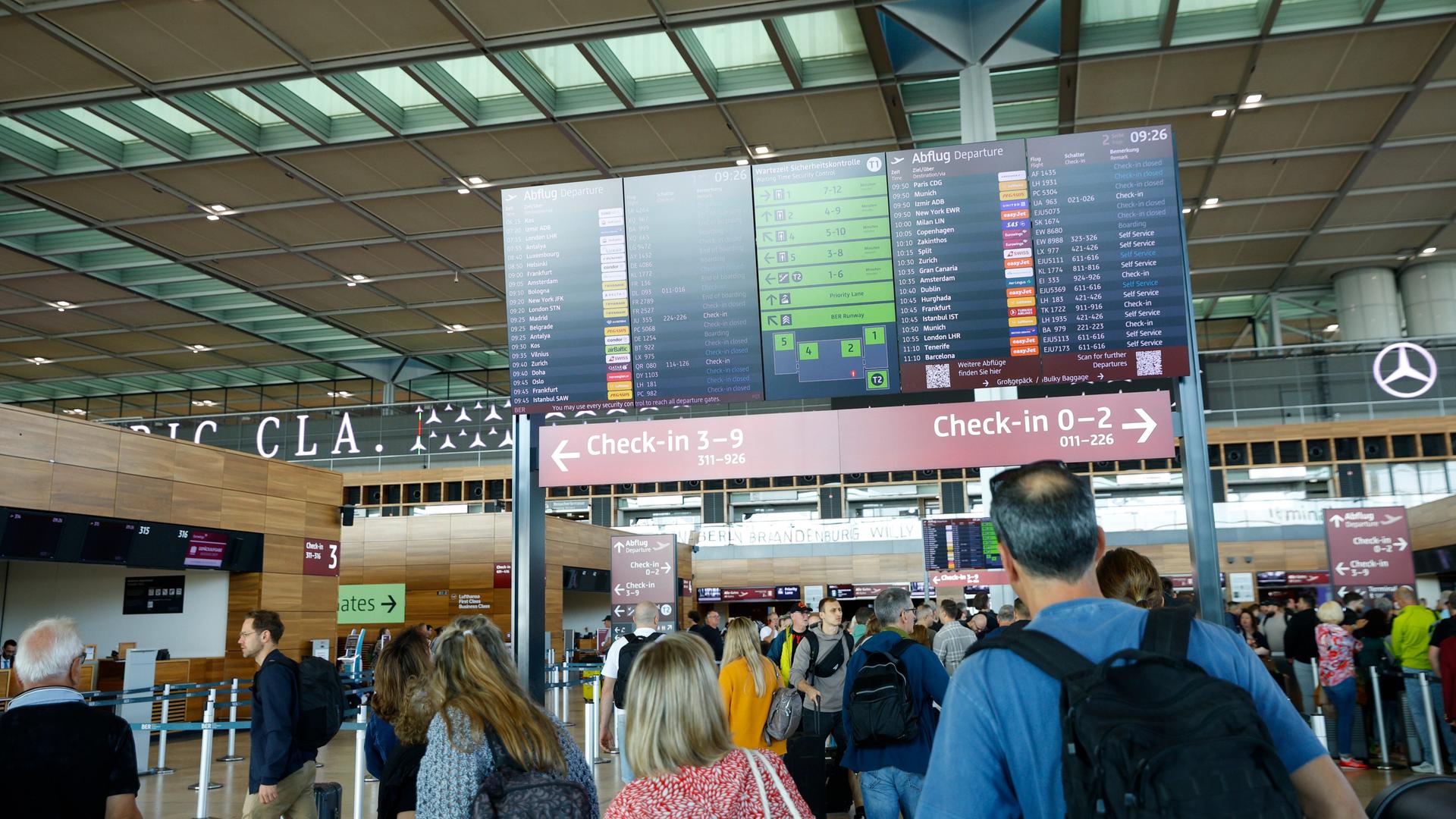 Menschen stehen in einer Halle des Berliner Flughafens BER und schauen auf eine Anzeigetafel. Menschen stehen in einer Halle des Berliner Flughafens BER und schauen auf eine Anzeigetafel.