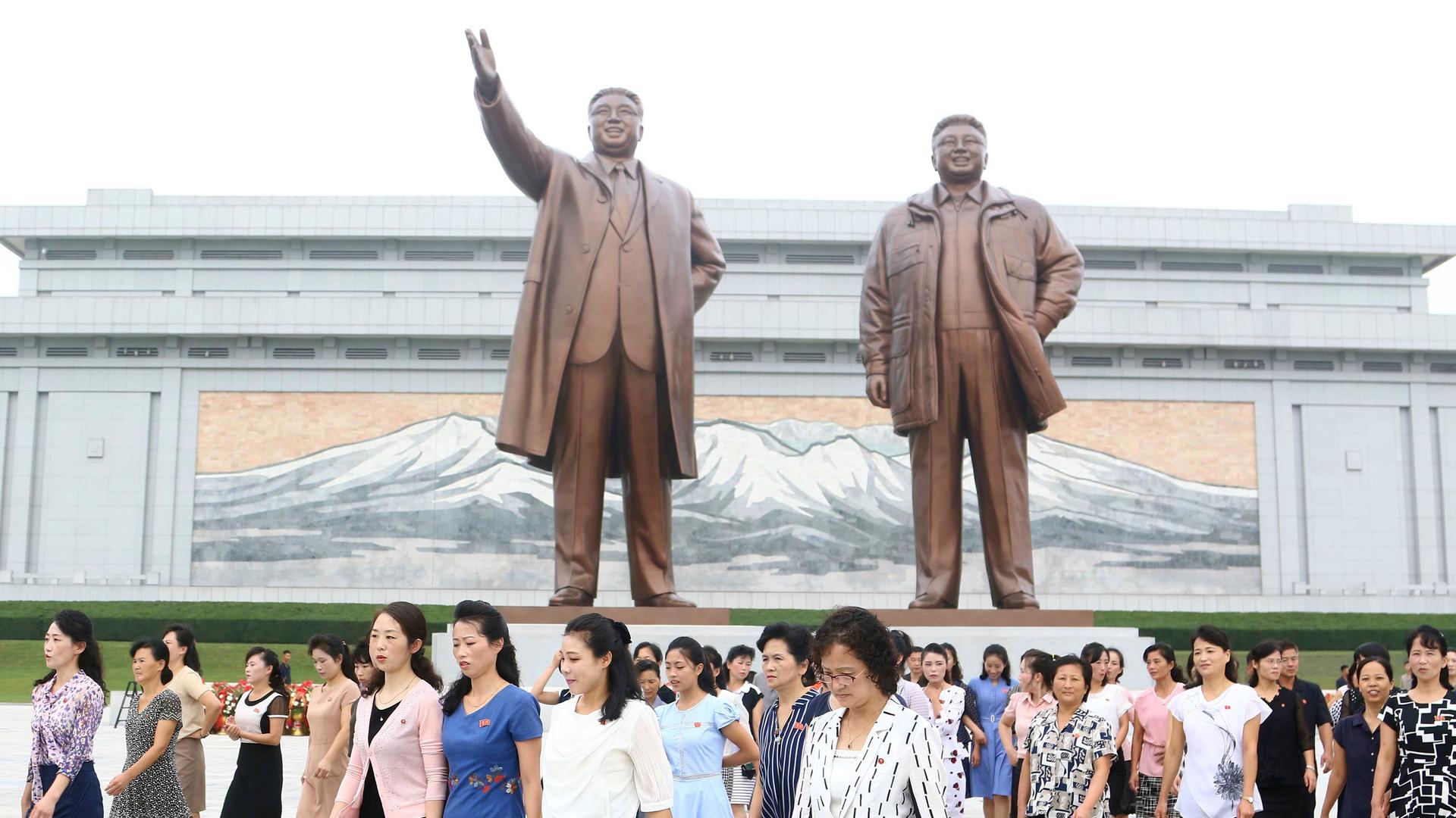 Menschen stehen neben großen, bronzefarbenen Statuen der ehemaligen nordkoreanischen Führer Kim Il Sung und Kim Jong Il.