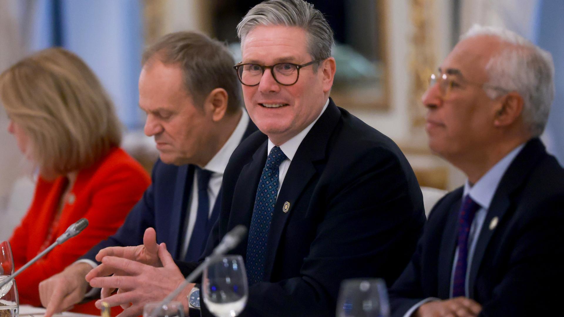 Starmer sitzt an einem Tisch zwischen weiteren Politikern. Vor ihm auf dem Tisch stehen Mikrofone. Starmer sitzt an einem Tisch zwischen weiteren Politikern. Vor ihm auf dem Tisch stehen Mikrofone.