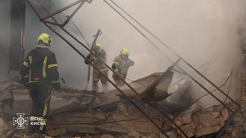 Das Bild zeigt mehrere Personen in Feuerwehr-Uniform in einem zerstörten Gebäude. Es sind Trümmer und viel Rauch zu sehen.