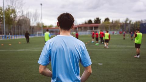 Ein Jugendlicher sieht seinen Teammitgliedern beim Fußballspielen zu.