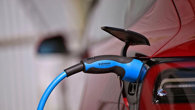 Öffentliche Ladesäule für E-Autos an einem Parkplatz. Ein Tesla Model 3 lädt gerade seinen Akku an der Stromtankstelle voll, der Stecker steckt im Ladeanschluss des Autos.