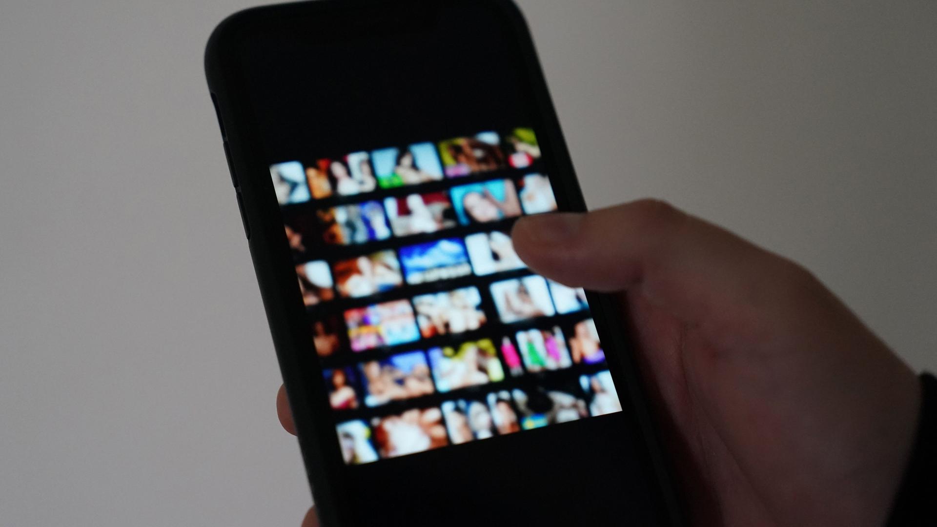 Eine Person hält ein Smartphone in der Hand. Darauf sind Porno-Inhalte zu sehen.