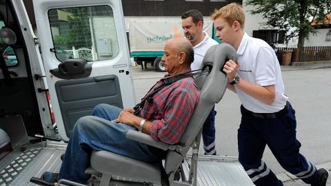 Ein junger Mann schiebt einen Rollstuhl mit einem Mann darauf in einen Transporter 