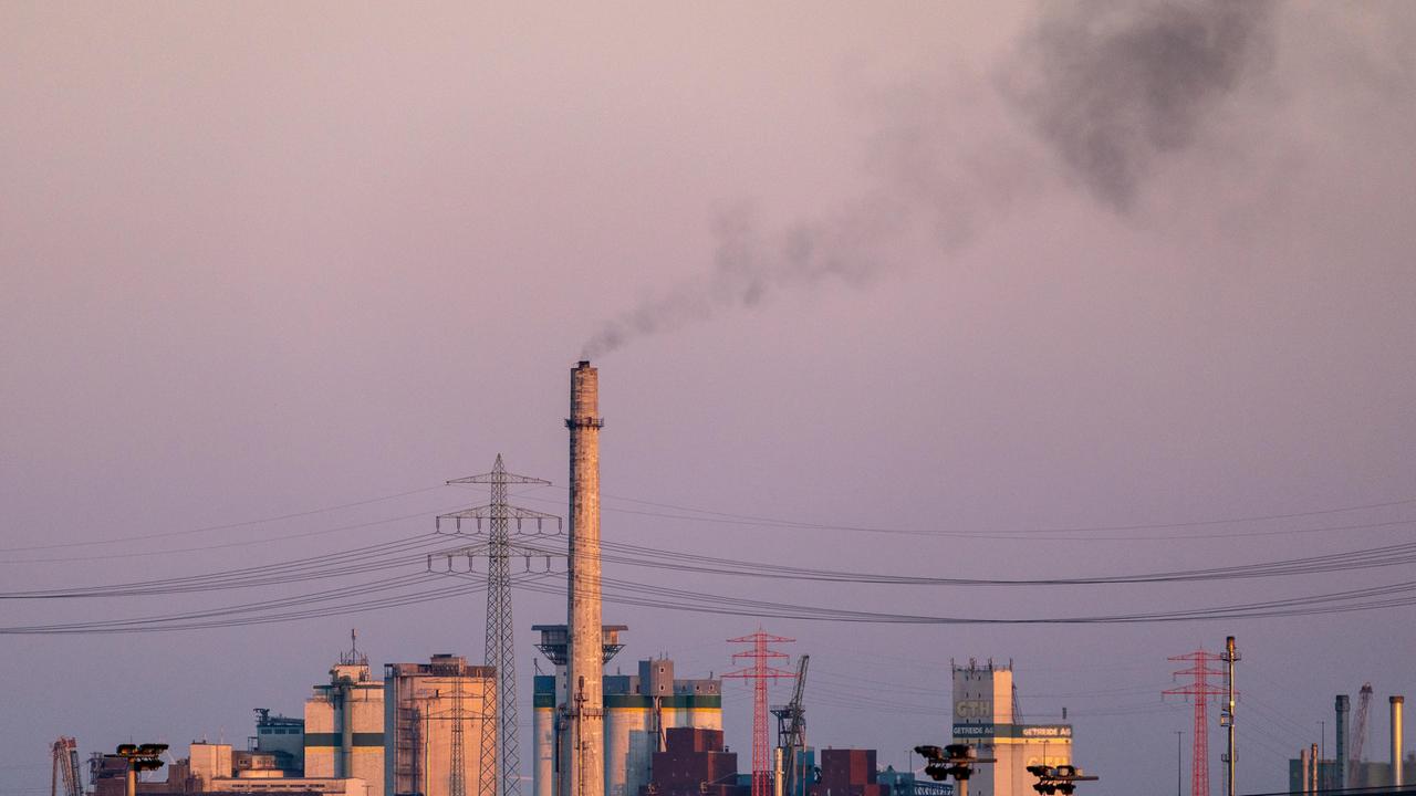 Ein hoher Industrieschornstein stößt bei Dämmerung dunkle Rauchwolken aus 