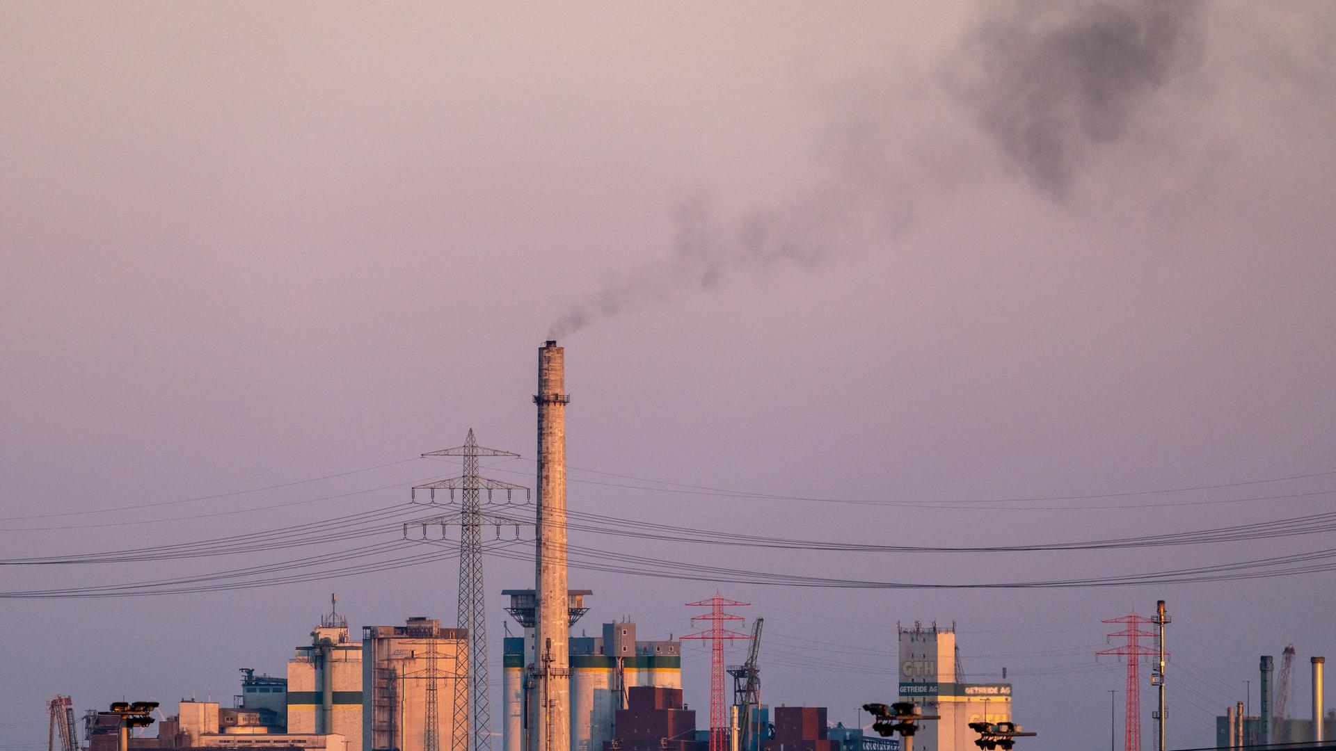 Ein hoher Industrieschornstein stößt bei Dämmerung dunkle Rauchwolken aus 