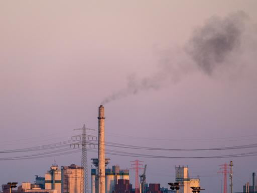 Ein hoher Industrieschornstein stößt bei Dämmerung dunkle Rauchwolken aus 