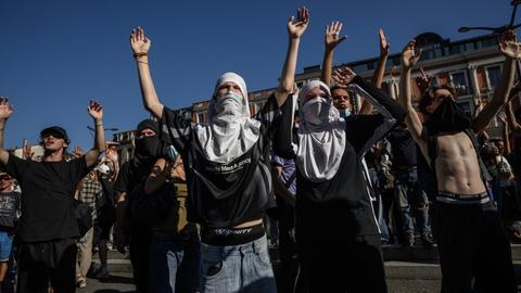 Teilweise vermummte Personen stehen auf einer Demonstration und heben ihre Hände in die Luft Teilweise vermummte Personen stehen auf einer Demonstration und heben ihre Hände in die Luft