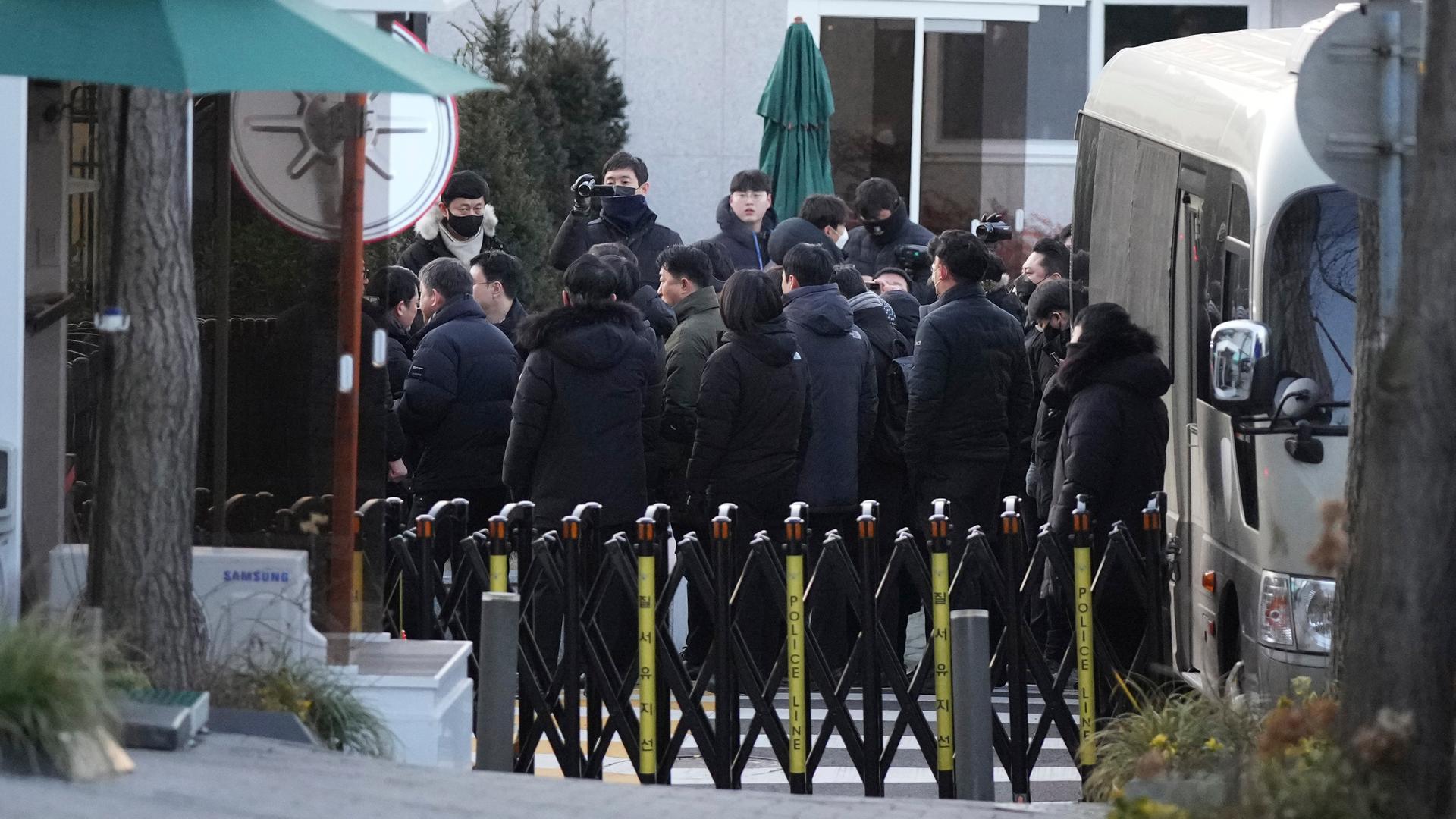 Zu sehen sind Staatsbedienstete, die sich vor der südkoreanischen Präsidentenresidenz sammeln. Im Vordergrund sind weiträumige Absperrungen zu sehen.