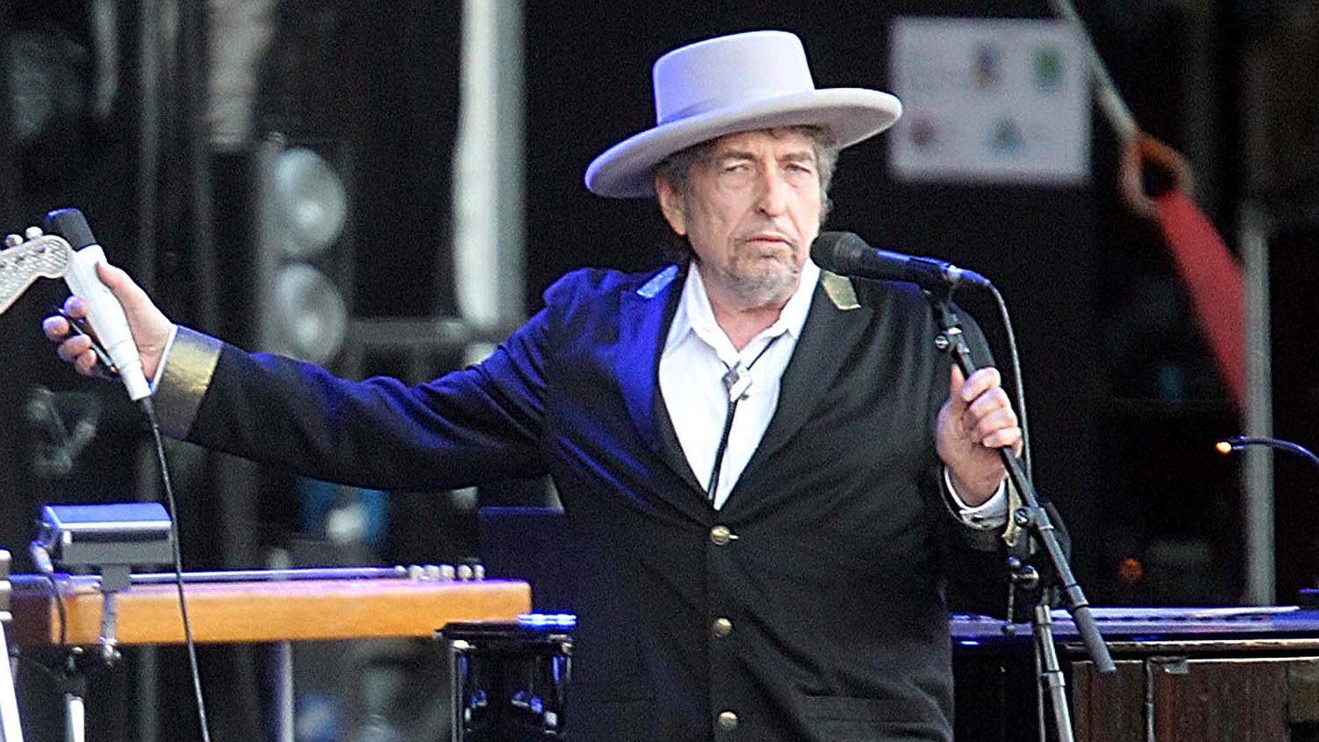 Ein Mann steht in Anzug und Hut auf der Bühne und hält ein Mikrofon in jeder Hand.