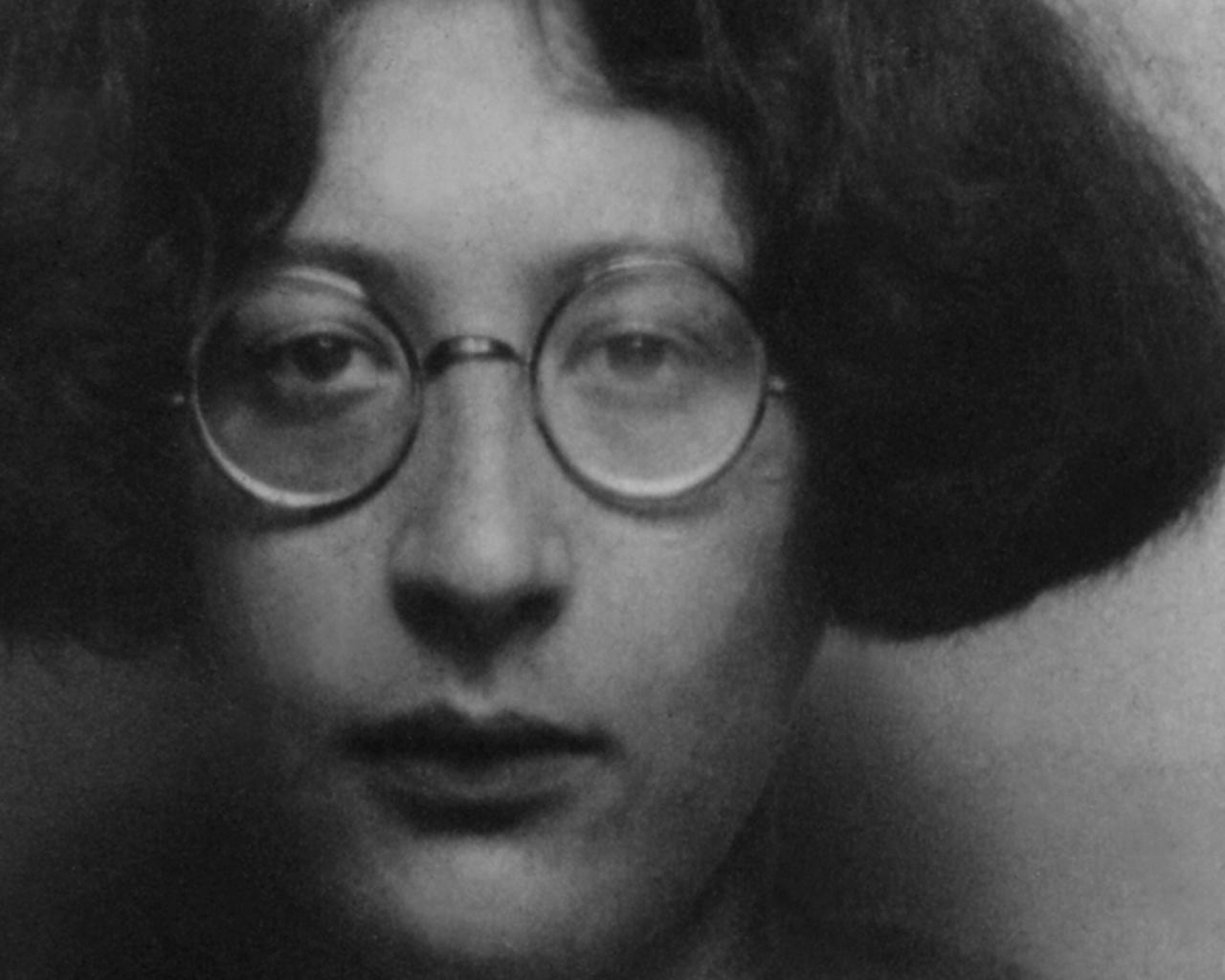 Schwarzweißfoto der Philosophin Simone Weil. Eine junge Frau mit halblangen dunklen Haaren und einer runden Brille. 