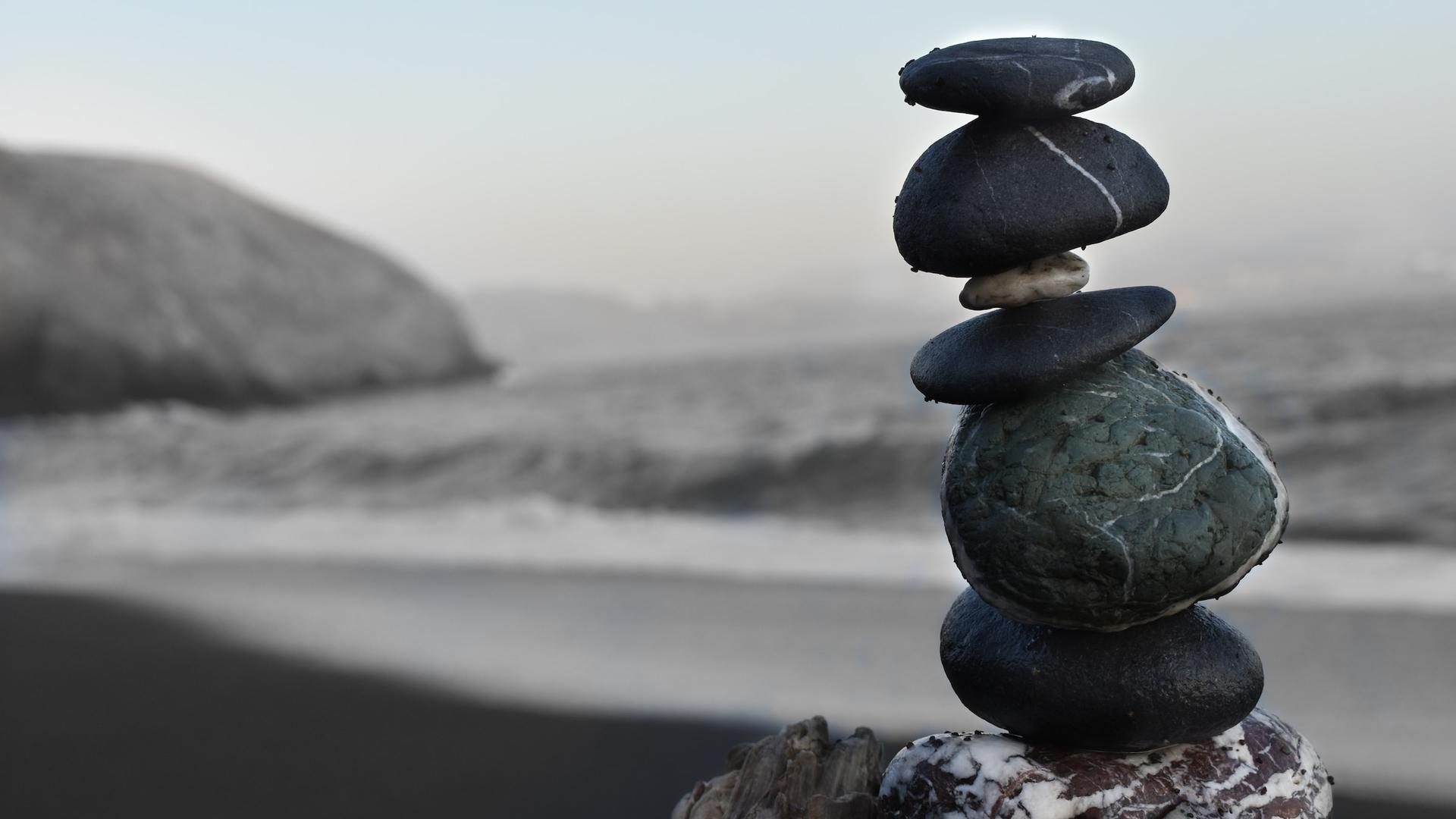 Aufeinander balancierende Steine bilden einen kleinen Turm an einem Strand. 