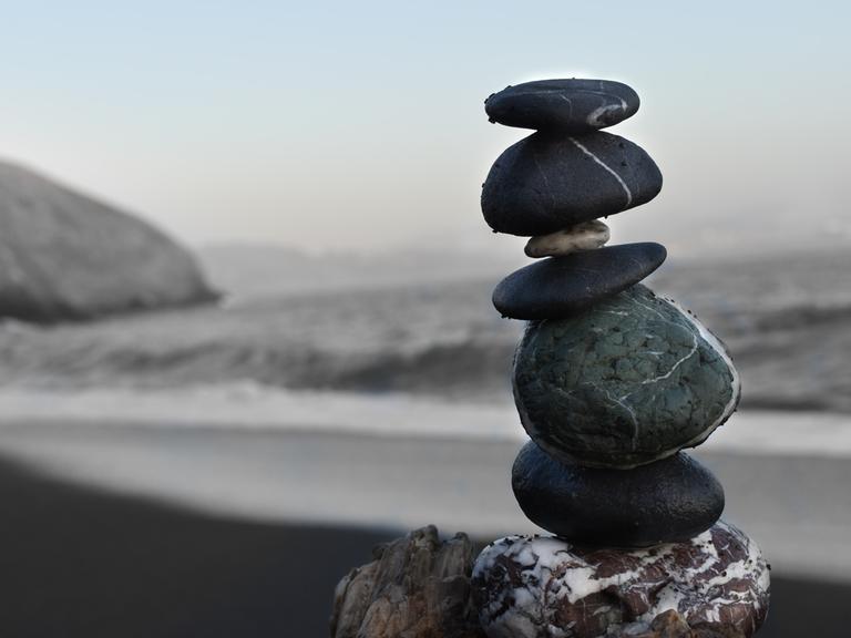 Aufeinander balancierende Steine bilden einen kleinen Turm an einem Strand. 