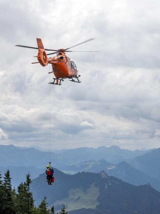 Ein Rettungshubschrauber in den Alpen, der an einem Seil zwei Personen transportiert.