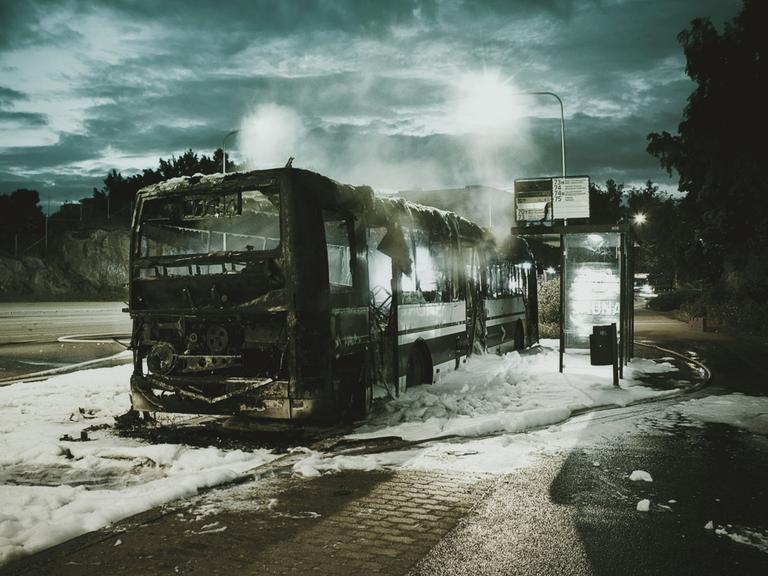 Ein ausgebrannter Autobus steht an einer Bushaltestelle