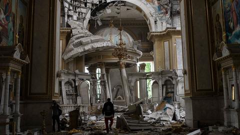 Kirchenmitarbeiter inspizieren die Schäden in der Verklärungskathedrale in Odessa nach russischen Raketenangriffen. Mauerteile sind heruntergefallen, Kuppeln zerstört, der Boden ist voller Trümmer.