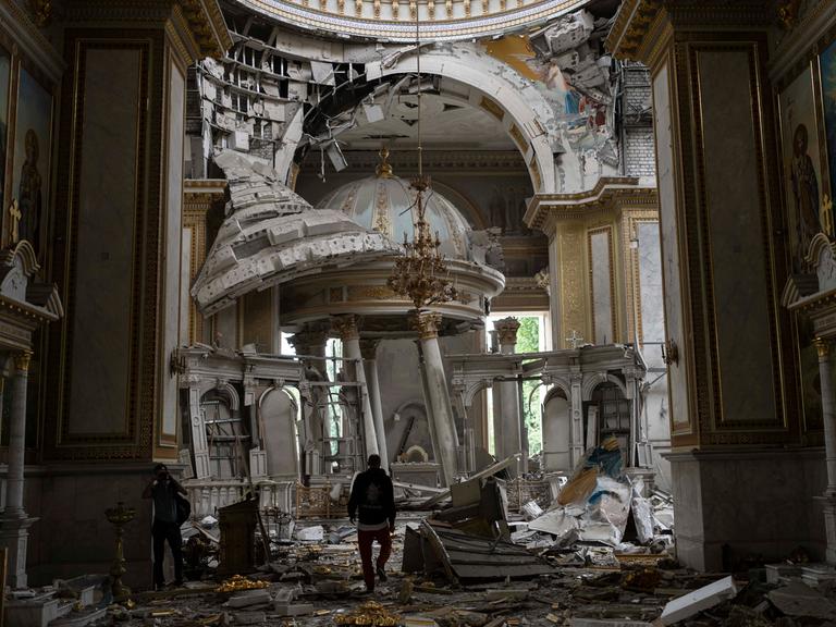 Kirchenmitarbeiter inspizieren die Schäden in der Verklärungskathedrale in Odessa nach russischen Raketenangriffen. Mauerteile sind heruntergefallen, Kuppeln zerstört, der Boden ist voller Trümmer.