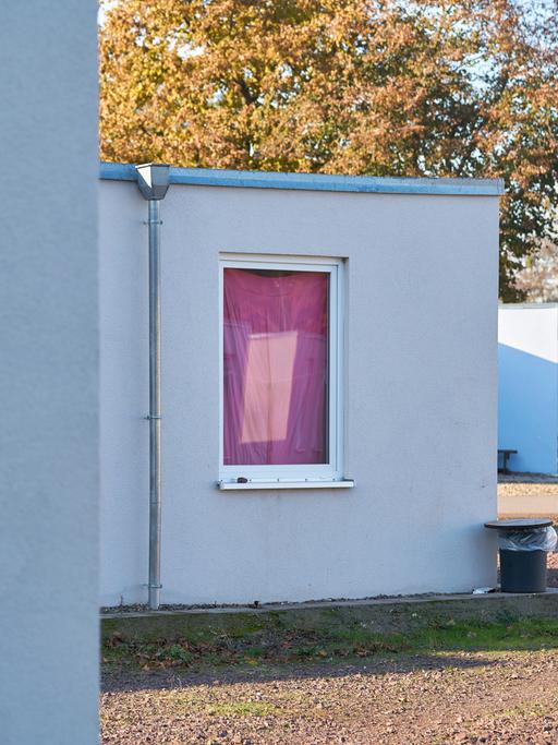 Blick auf einen Flachbau mit provisorisch verhangenem Fenster auf dem Gelände einer Flüchtlingsunterkunft.