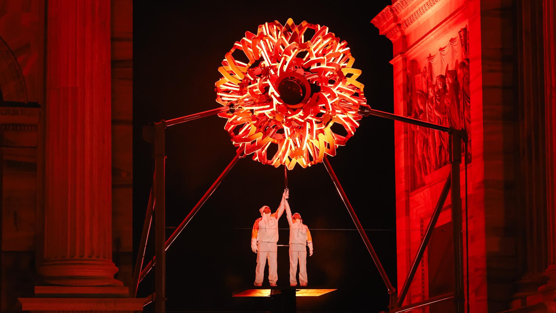 Zwei italienische Sportler halten eine Fackel. Oben zu sehen ist das olympische Feuer.