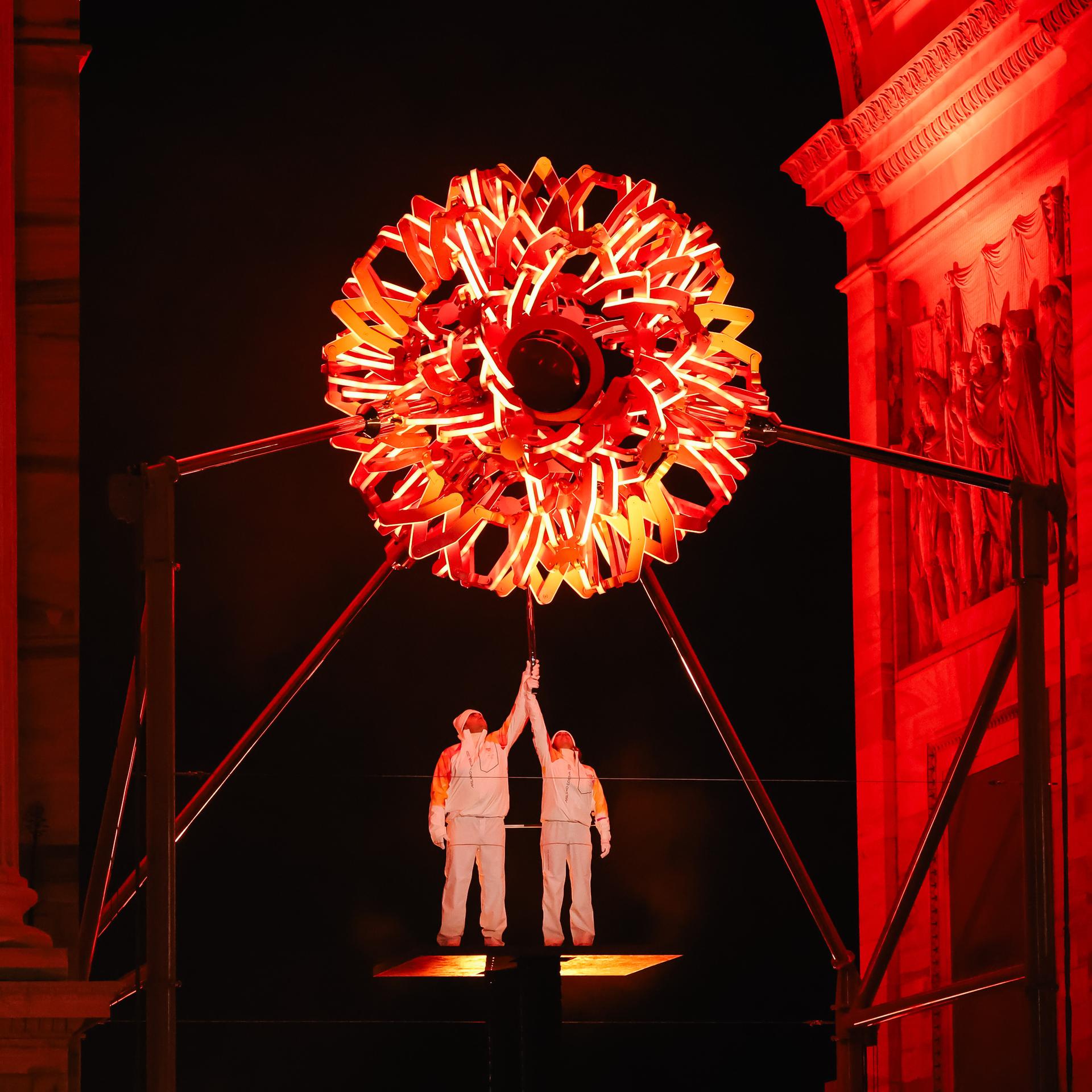 Zwei italienische Sportler halten eine Fackel. Oben zu sehen ist das olympische Feuer.