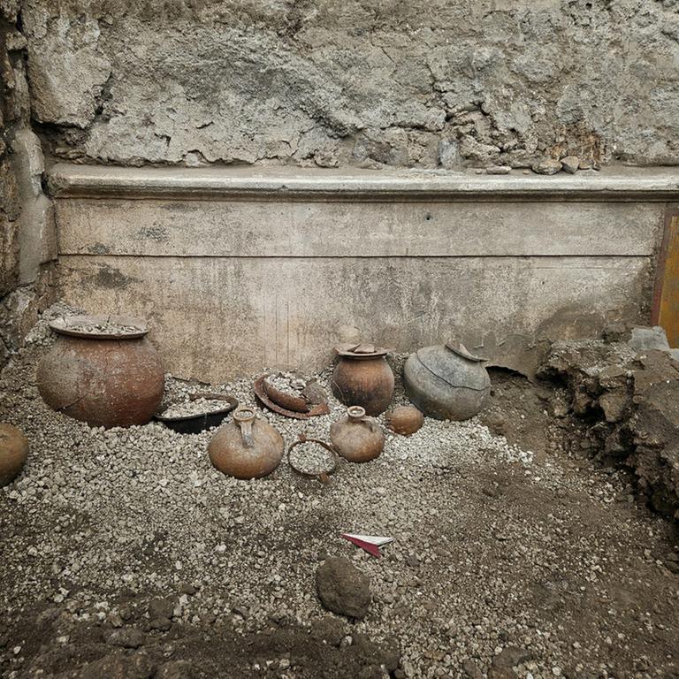 Töpfe und Amphoren mit Münzen und Resten von Kosmetika stehen in einem Raum in Pompeji