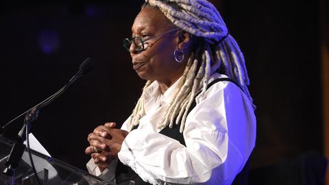 Whoopi Goldberg steht an einem Rednerpult und spricht ins Mikrofon
