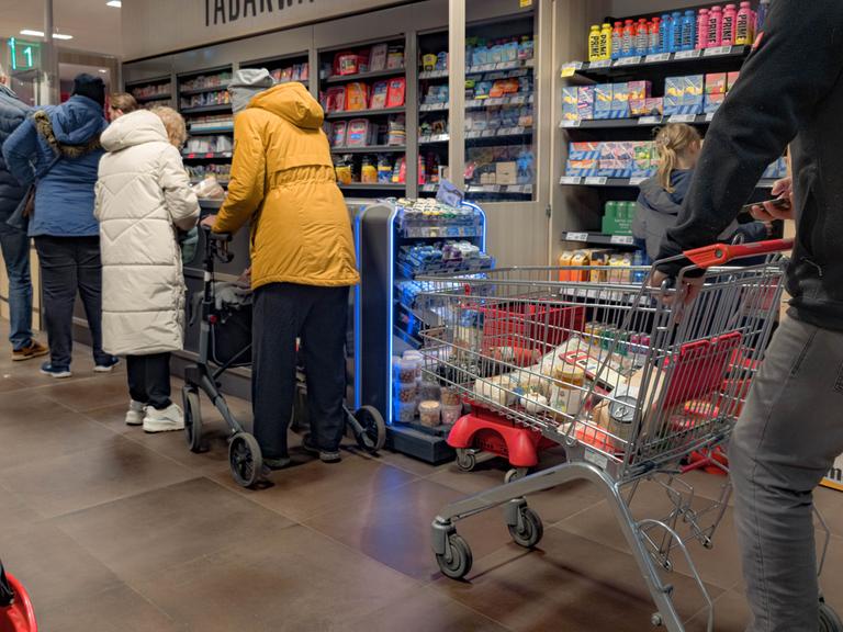 Kunden warten in einem Supermarkt an der Kasse.