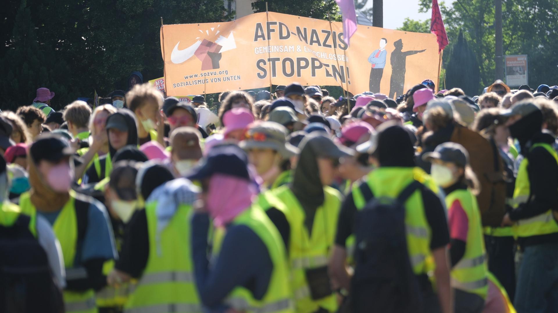 Ein Pulk von Demonstrierenden in Warnwesten; auf einem großen Banner steht "AfD-Nazis stoppen". Ein Pulk von Demonstrierenden in Warnwesten; auf einem großen Banner steht "AfD-Nazis stoppen".