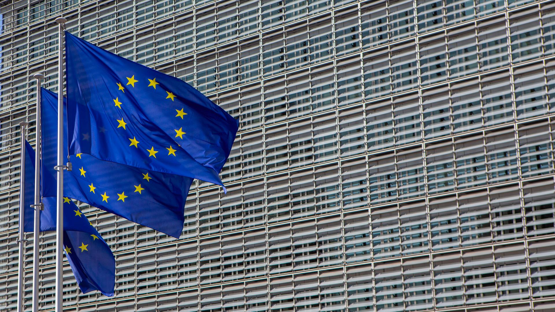 Das Berlaymont-Gebäude in Brüssel, der Sitz der Europäischen Kommission. Davor wehen drei Europafahnen. 