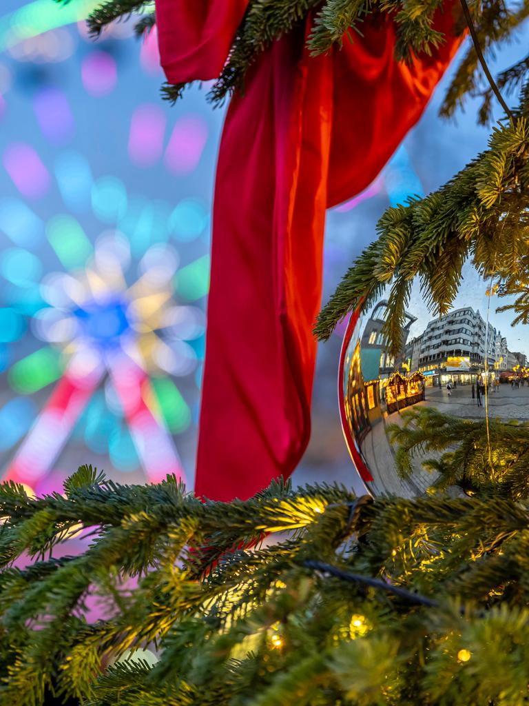 Buden spiegeln sich in einer Weihnachtskugel. Im Hintergrund: ein Riesenrad.