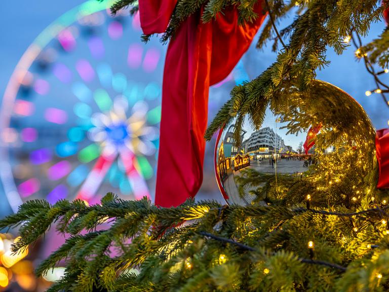 Buden spiegeln sich in einer Weihnachtskugel. Im Hintergrund: ein Riesenrad.