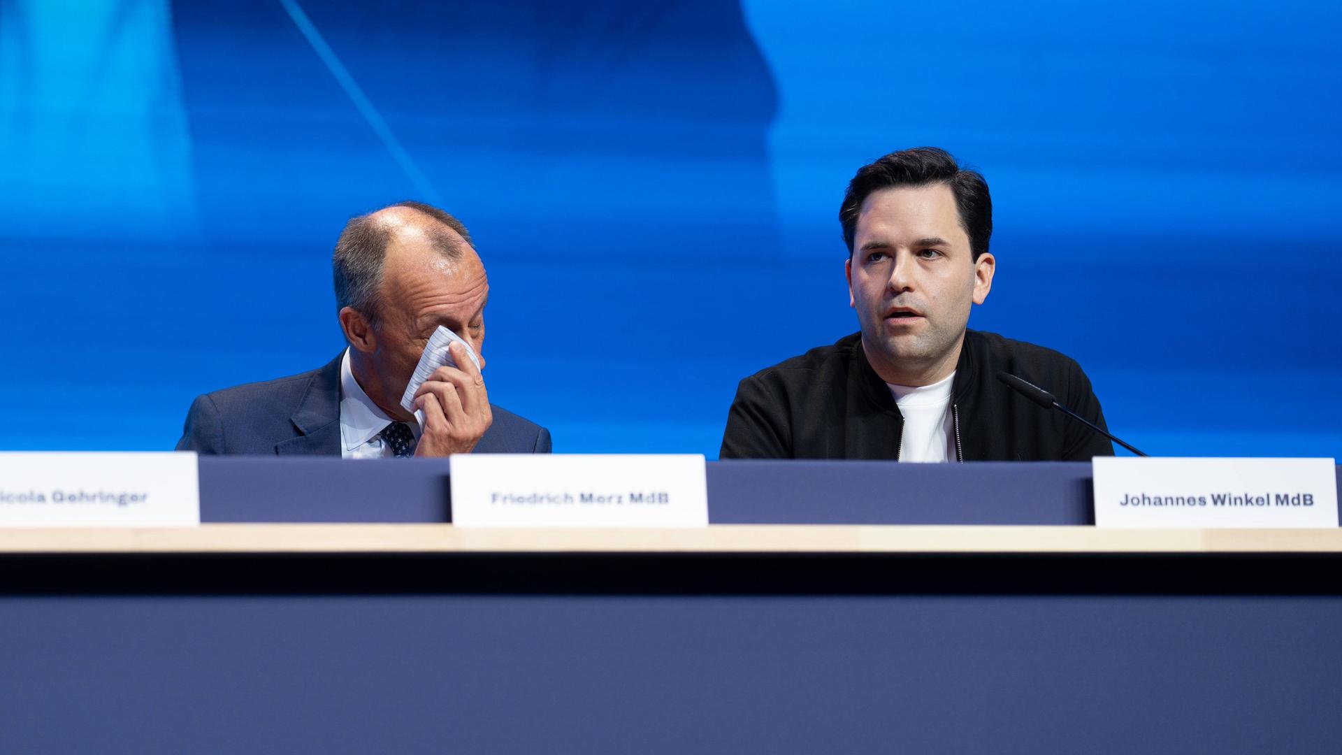 Friedrich Merz sitzt auf einem Podium neben dem Vorsitzenden der Jungen Union Johannes Winkel und tupft sich mit einem Tuch Schweiß von der Stirn. Friedrich Merz sitzt auf einem Podium neben dem Vorsitzenden der Jungen Union Johannes Winkel und tupft sich mit einem Tuch Schweiß von der Stirn.