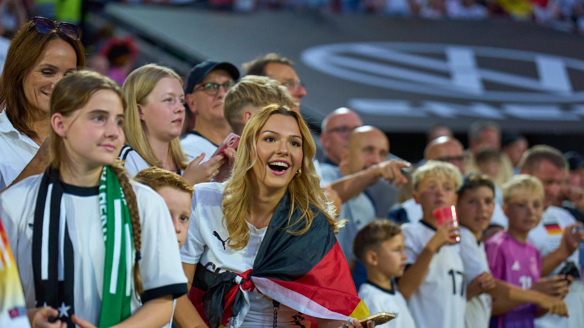 Deutsche Fußball-Fans beim WM-Qualifikationsspiel gegen Nordirland. Im MIttelpunkt von dem Bild ist eine junge Frau mit langen Haaren. Sie freut sich.