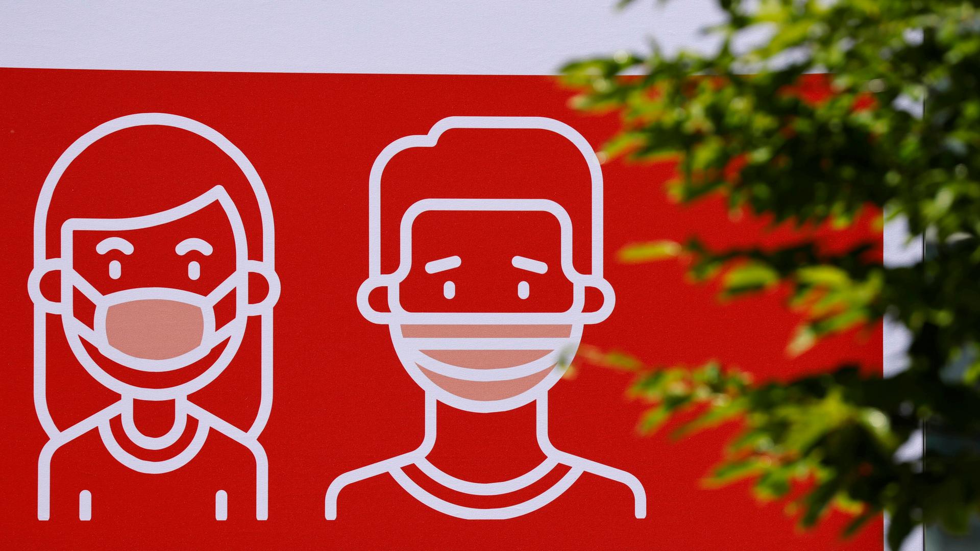 Auf einem Schild sind zwei Figuren zu sehen, die eine Schutz-Maske tragen.  