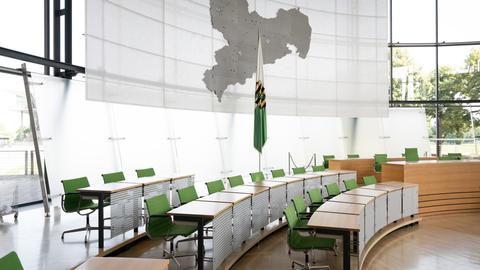 Leere Stühle an der Regierungsbank im Plenarsaal des Landtag. Dahinter steht die sächsische Landesflagge und ein Umriss des Bundeslandes an der Wand.