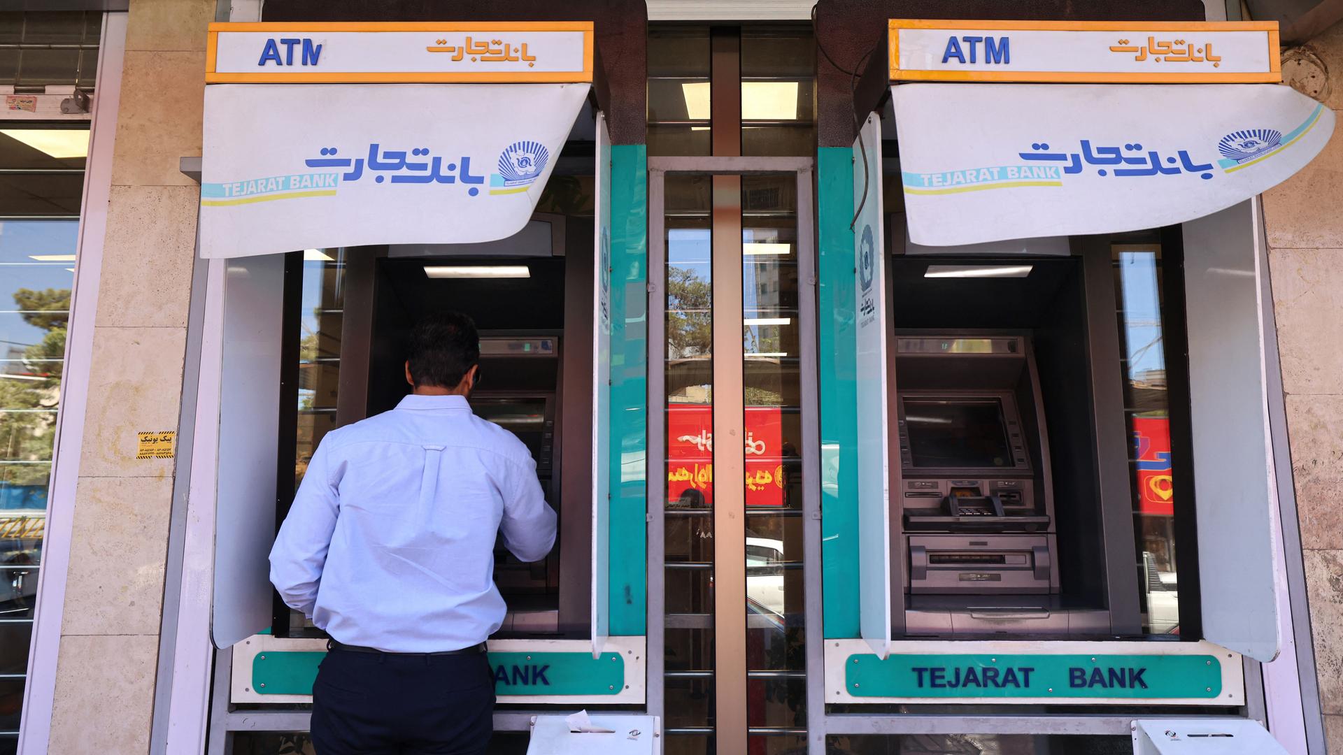 Geldautomat der Tejarat Bank in der iranischen Hauptstadt Teheran. Vor dem Geldautomaten steht ein Mann in dunkler Hose und blauem Hemd. Geldautomat der Tejarat Bank in der iranischen Hauptstadt Teheran. Vor dem Geldautomaten steht ein Mann in dunkler Hose und blauem Hemd.