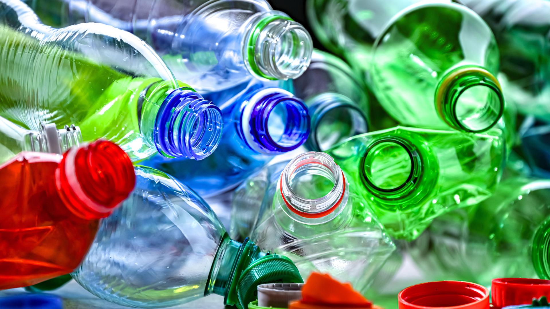 Leere Plastiflaschen in verschiedenen Farben liegen durcheinander. Die Flaschen sind geöffnet, die Flaschendeckel hängen an den Öffnungen.