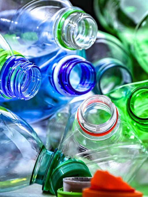 Leere Plastiflaschen in verschiedenen Farben liegen durcheinander. Die Flaschen sind geöffnet, die Flaschendeckel hängen an den Öffnungen.