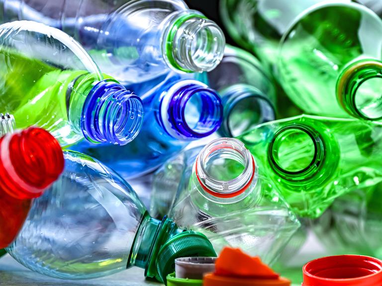 Leere Plastiflaschen in verschiedenen Farben liegen durcheinander. Die Flaschen sind geöffnet, die Flaschendeckel hängen an den Öffnungen.