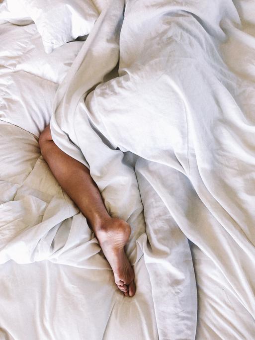 Ein Mann schläft in einem weissen Bett, das nackte Bein schaut unter der Decke hervor.