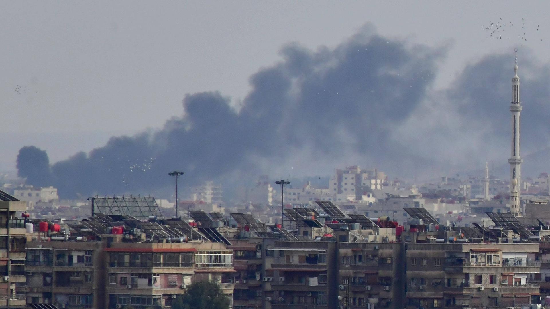 Rauch steigt am Horizont hinter Häusern der syrischen Hauptstadt Damaskus auf.