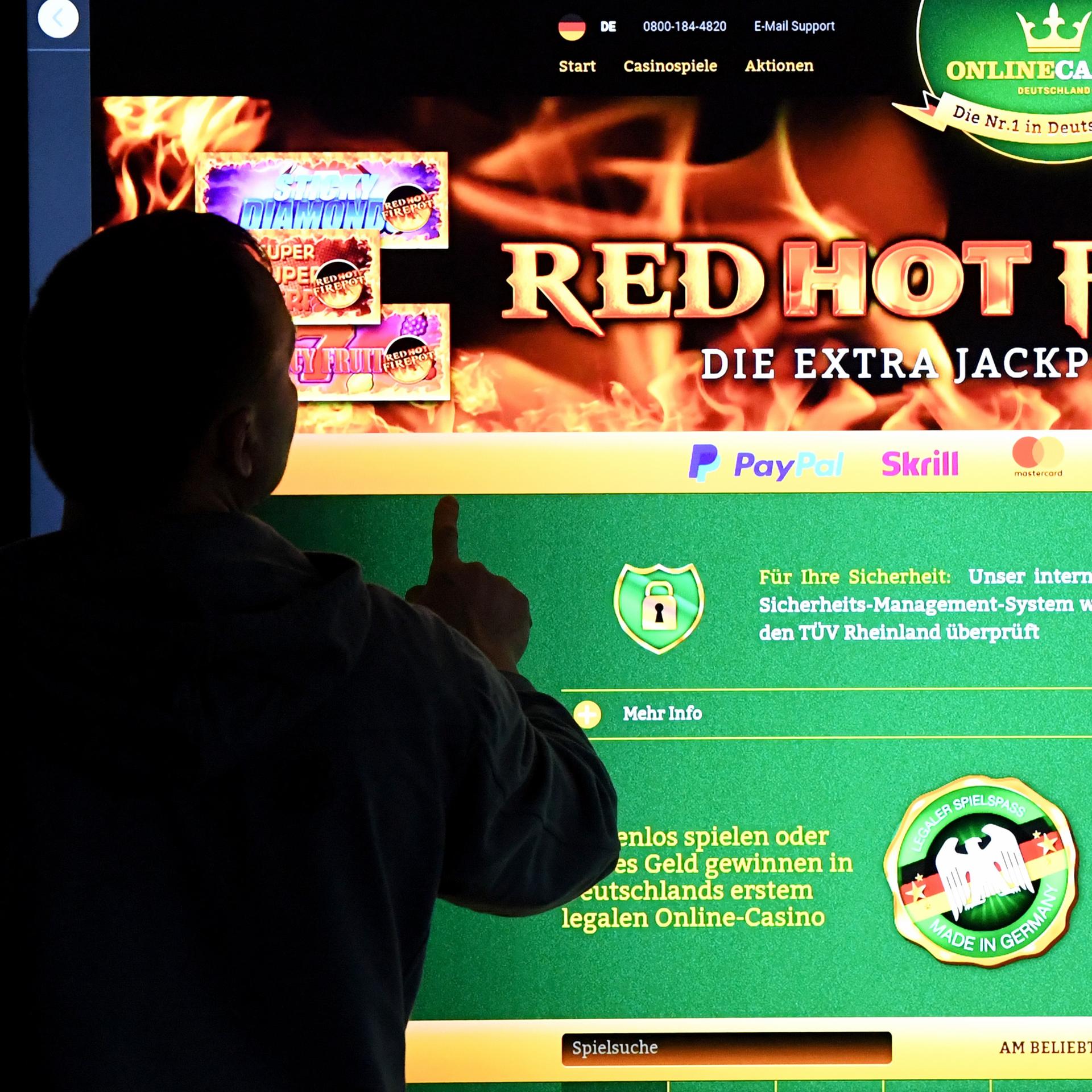Ein Mann steht vor einem Bildschirm mit einer Seite eines Anbieters für Online-Glückspiel (OnlineCasino)