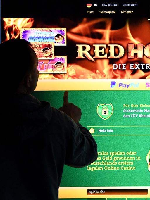 Ein Mann steht vor einem Bildschirm mit einer Seite eines Anbieters für Online-Glückspiel (OnlineCasino) Ein Mann steht vor einem Bildschirm mit einer Seite eines Anbieters für Online-Glückspiel (OnlineCasino)