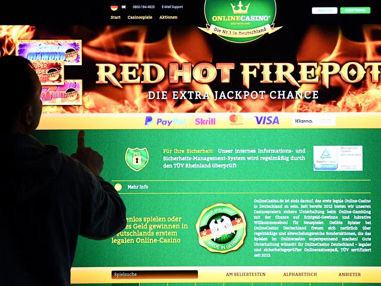 Ein Mann steht vor einem Bildschirm mit einer Seite eines Anbieters für Online-Glückspiel (OnlineCasino) Ein Mann steht vor einem Bildschirm mit einer Seite eines Anbieters für Online-Glückspiel (OnlineCasino)