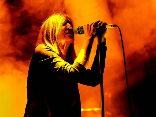 Beth Gibbons steht hinter einem Mikrophon einer grell orange-gelb beleuchteten Bühne.