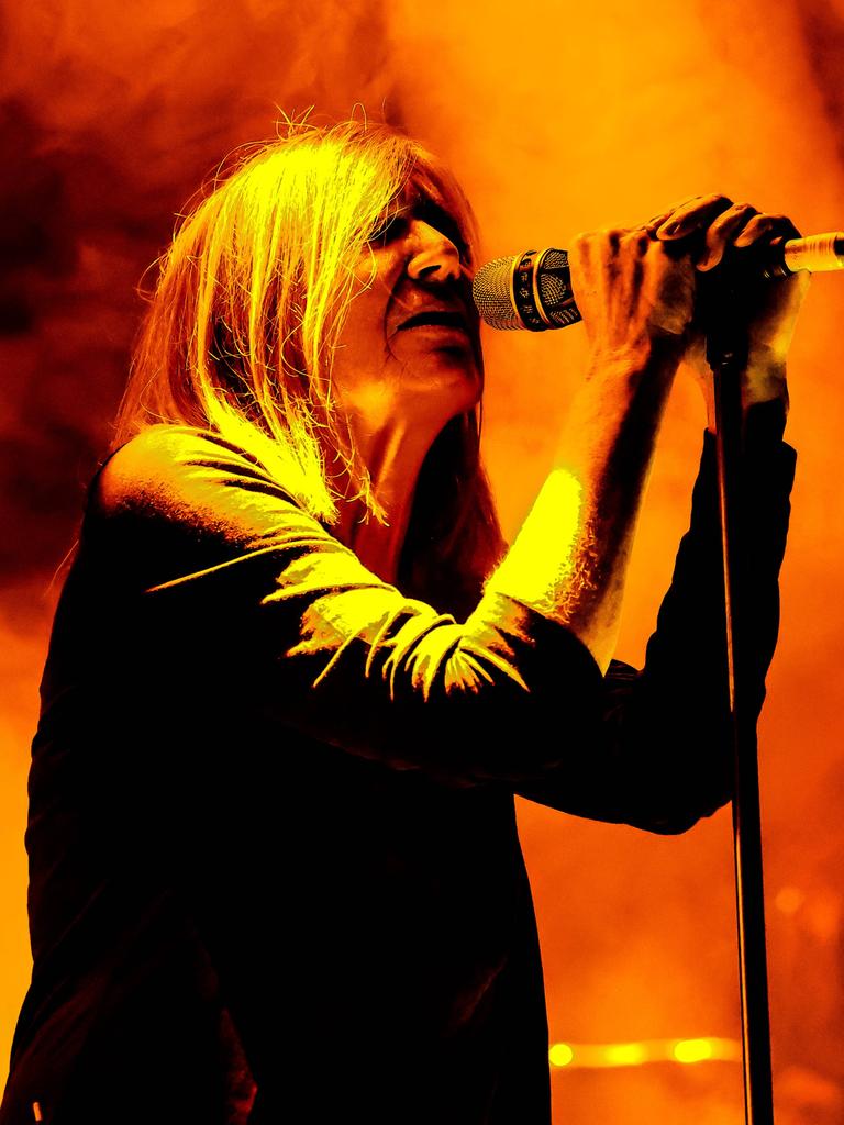 Beth Gibbons steht hinter einem Mikrophon einer grell orange-gelb beleuchteten Bühne.