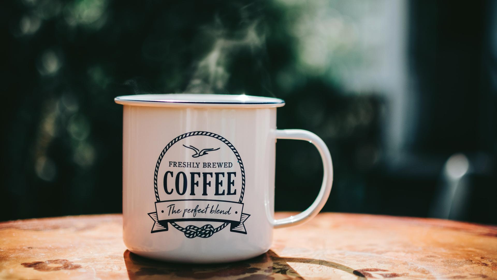 Eine dampfende Kaffeetasse steht auf einem braunen Tisch.