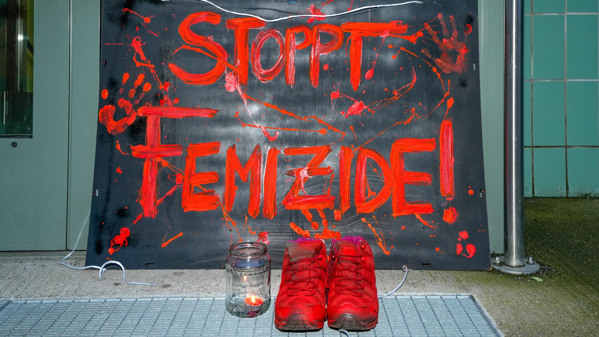 Berlin, vor der Eingangstuer des Mädchenzentrums Szenenwechsel in Berlin-Neukölln steht ein Schild mit der Aufschrift "STOPPT FEMIZIDE!" in Orang.  Dazu steht ein paar Schuhe, ebenalls in Orange und ein Teelicht mit brennender Kerze.