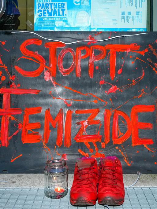 Berlin, vor der Eingangstuer des Mädchenzentrums Szenenwechsel in Berlin-Neukölln steht ein Schild mit der Aufschrift "STOPPT FEMIZIDE!" in Orang.  Dazu steht ein paar Schuhe, ebenalls in Orange und ein Teelicht mit brennender Kerze.