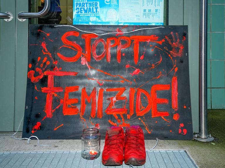 Berlin, vor der Eingangstuer des Mädchenzentrums Szenenwechsel in Berlin-Neukölln steht ein Schild mit der Aufschrift "STOPPT FEMIZIDE!" in Orang.  Dazu steht ein paar Schuhe, ebenalls in Orange und ein Teelicht mit brennender Kerze.